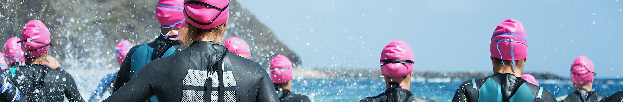 Group triathlon participants running into the water for swim portion of race,splash of water and athletes running
