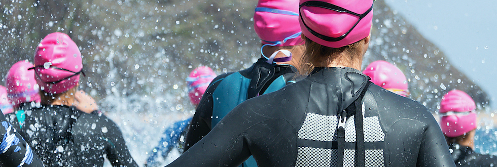 Group triathlon participants running into the water for swim portion of race,splash of water and athletes running